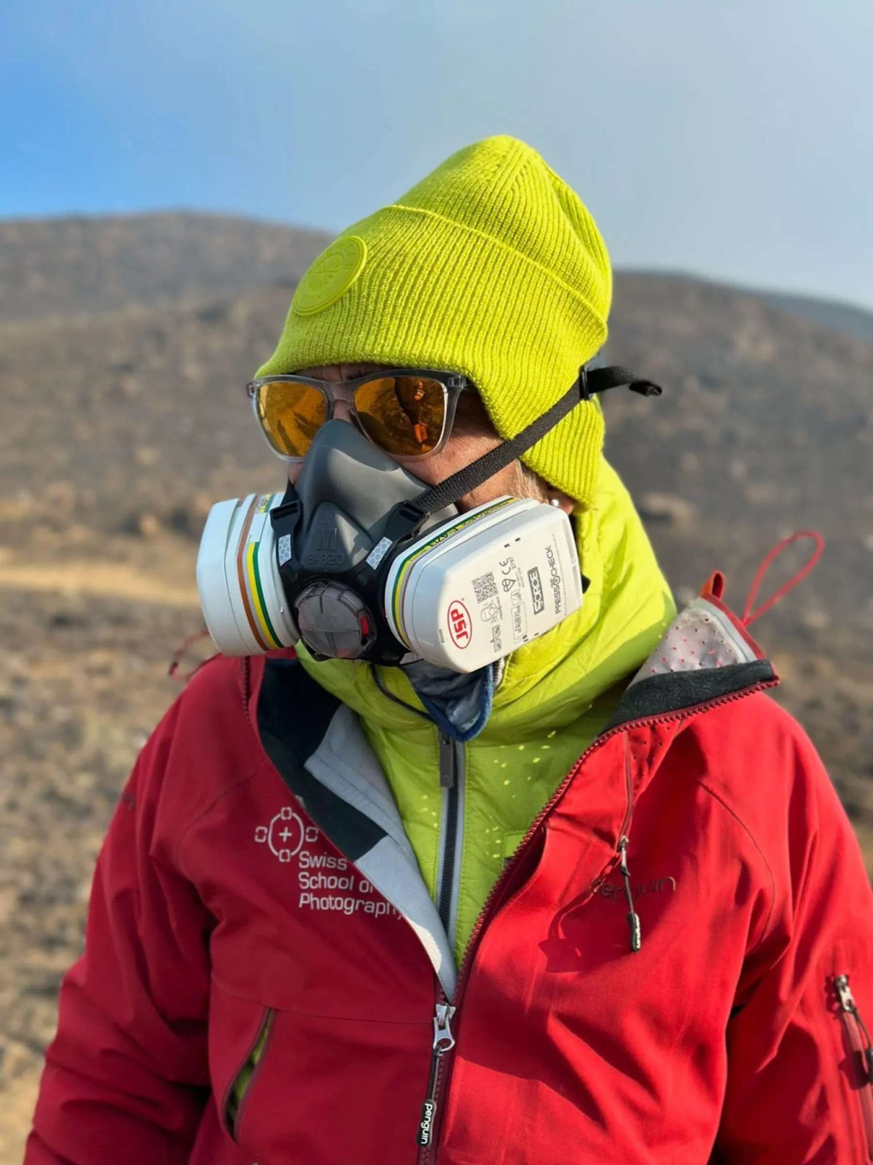 A photographer wearing a gas-mask respirator and safety gear near an active volcano in Iceland
