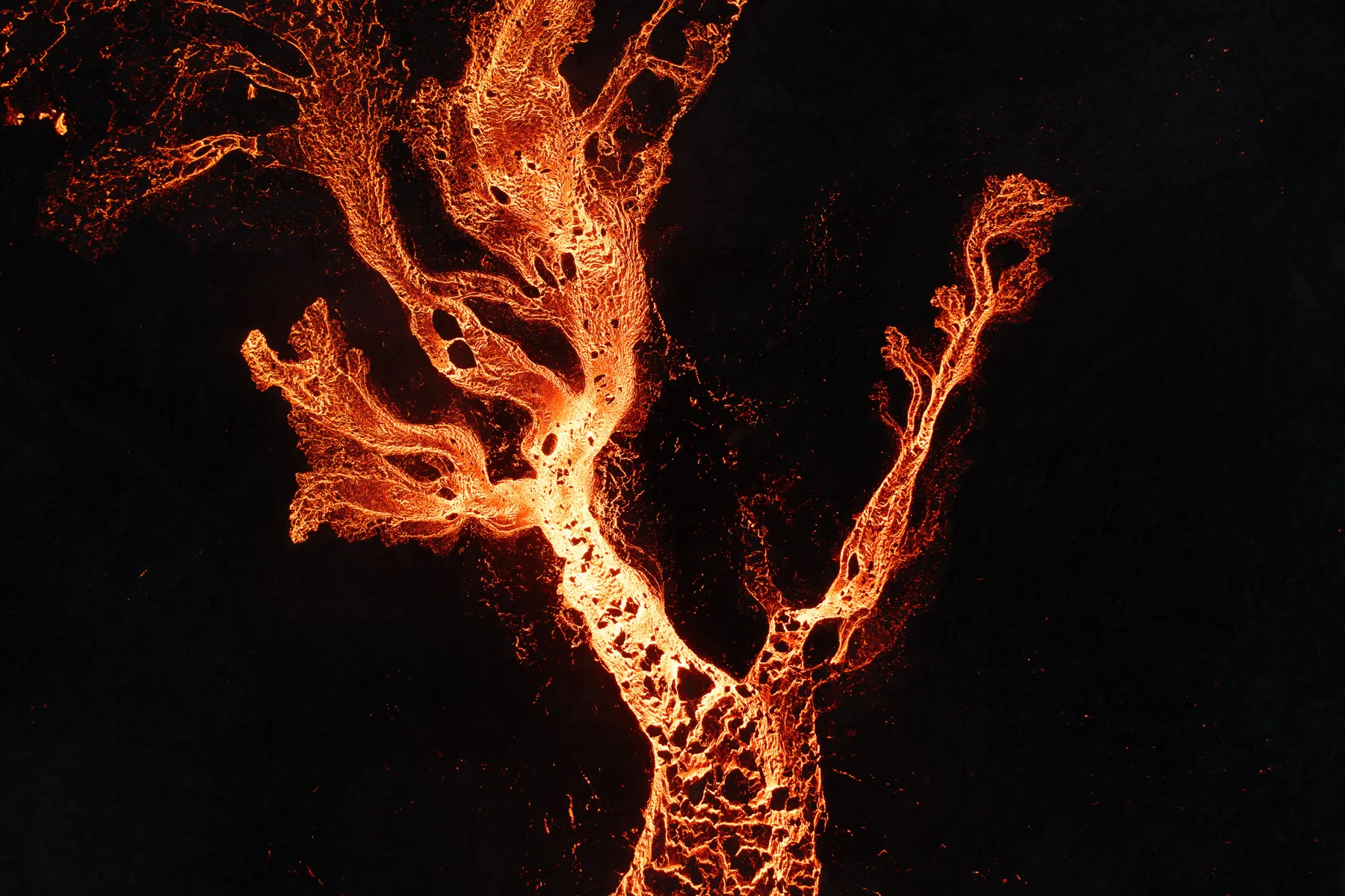 Aerial detail of glowing molten lava channels branching across dark ground in Iceland