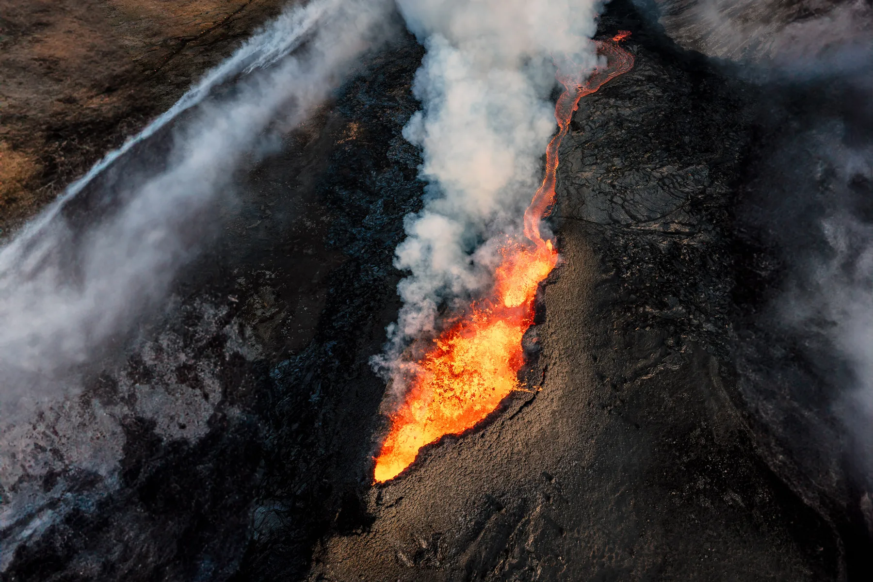 Aerial view of an active volcanic fissure with lava and a wall of steam venting in Iceland