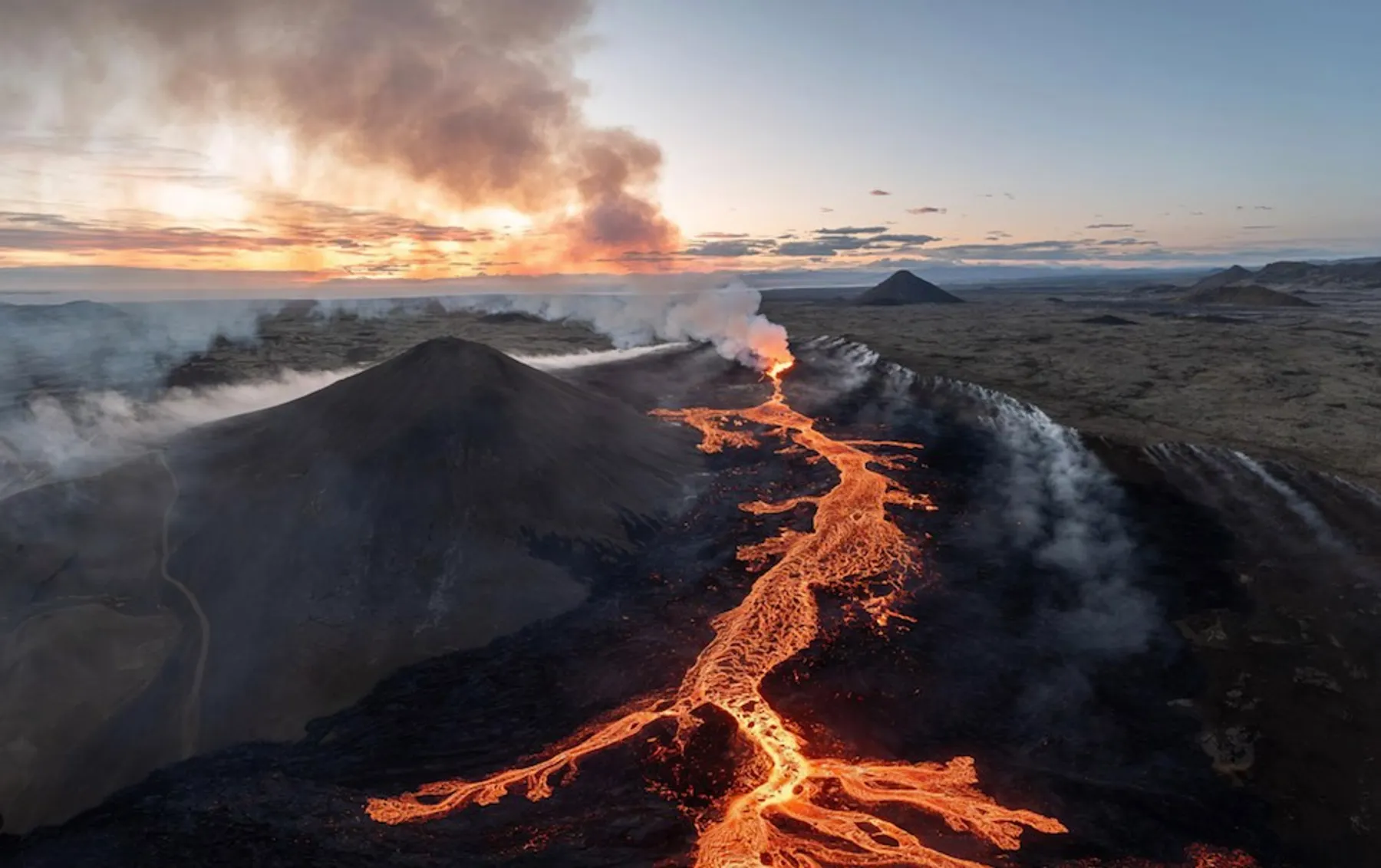 Aerial drone photograph of an active volcano erupting at sunset in Iceland, lava flowing across black rock