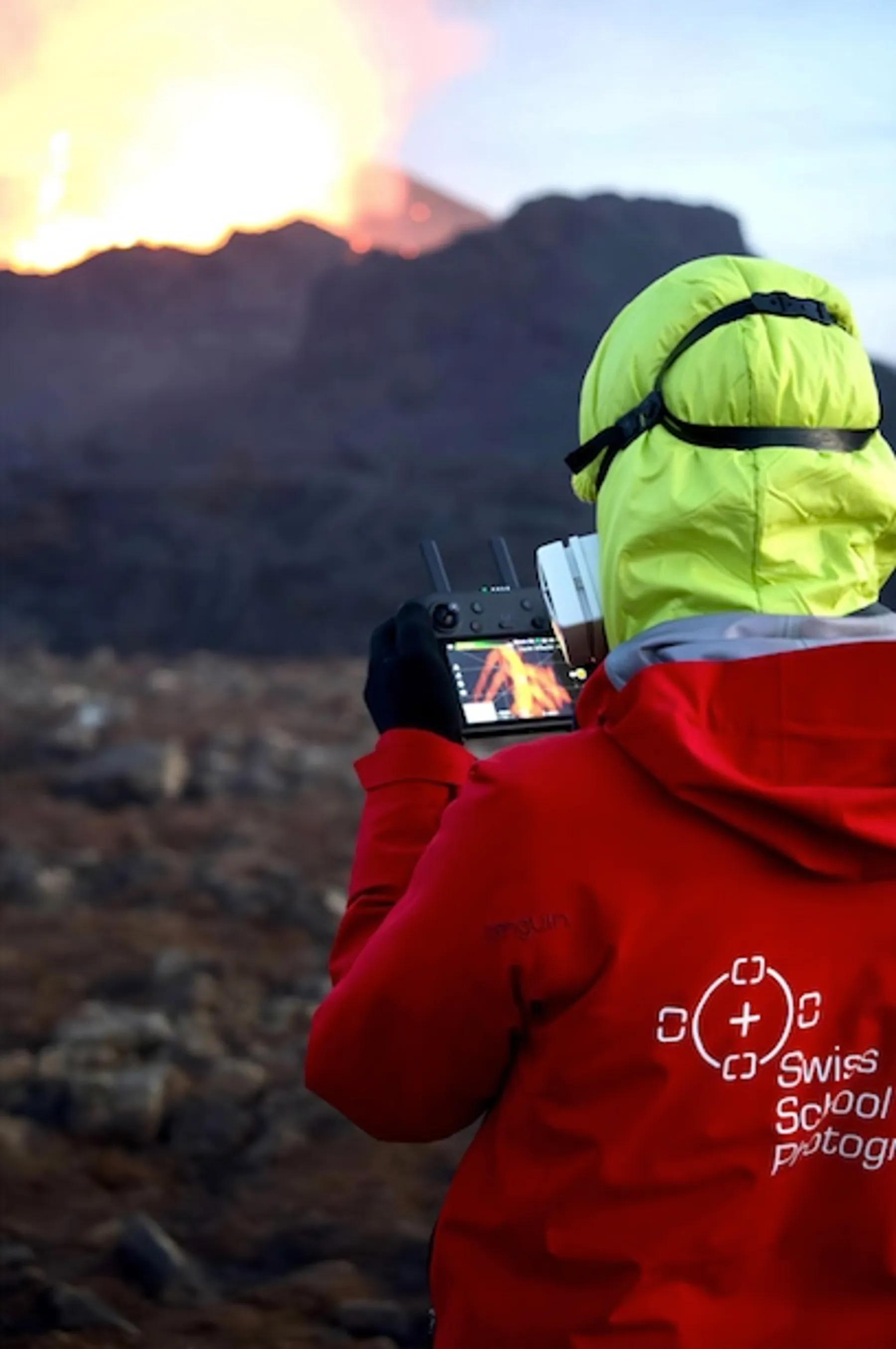 A photographer in a red Swiss School of Photography jacket photographing an erupting volcano in Iceland
