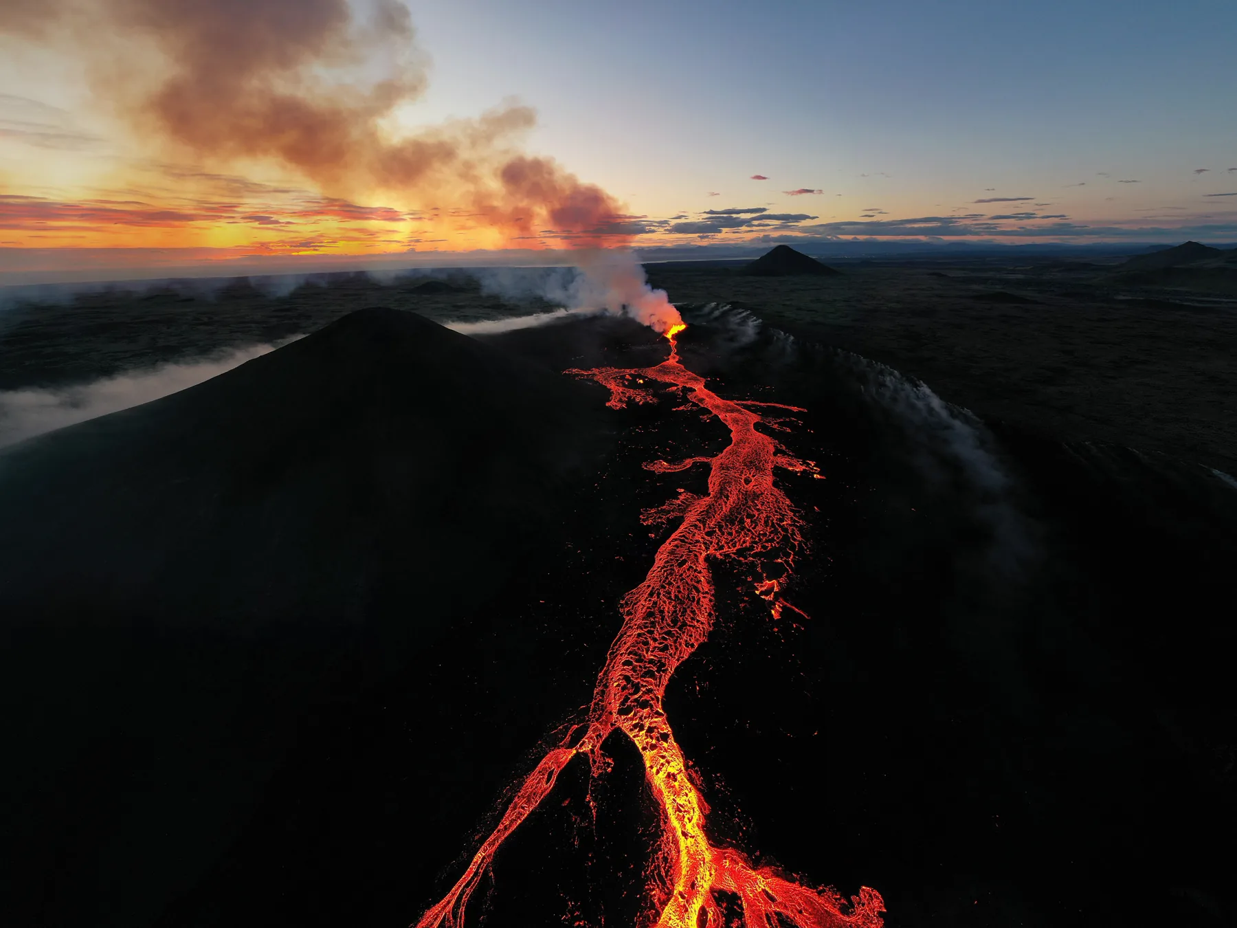 Golden sunset aerial of an erupting volcano with a lava river running down the slope in Iceland